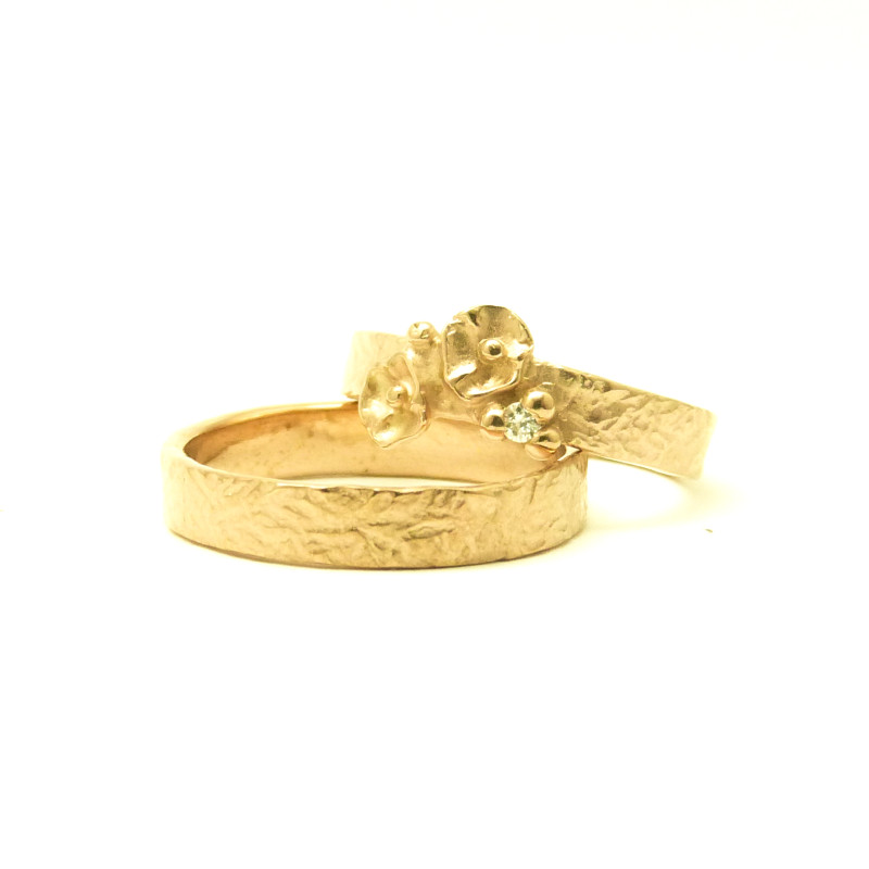 Gesmeden trouwringen in Rosé Goud. Haar ring draagt bloempjes en een diamantje.
